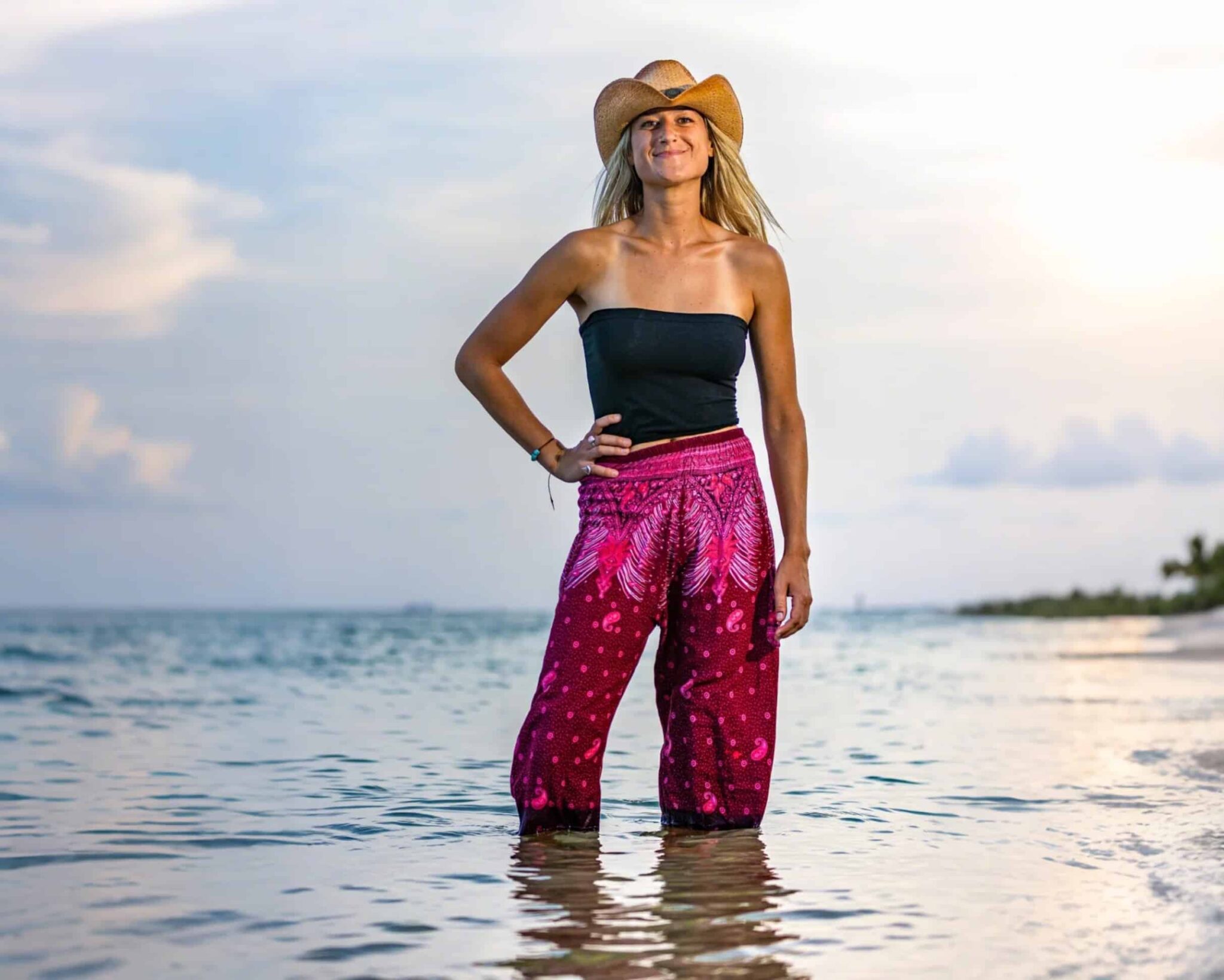 Woman standing in ocean wearing hat smiling.